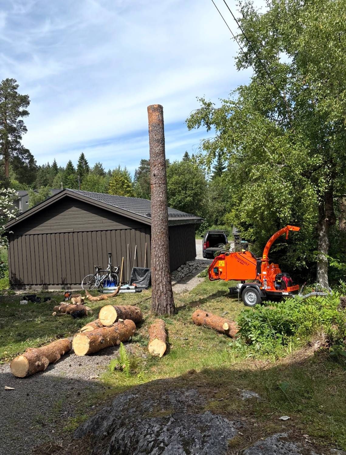 Tømmerstokker og flishugger på plenen ved siden av en garasje